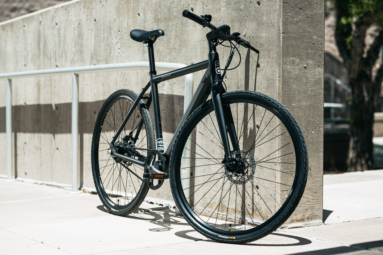 black hybrid bicycle leaning against a concrete wall